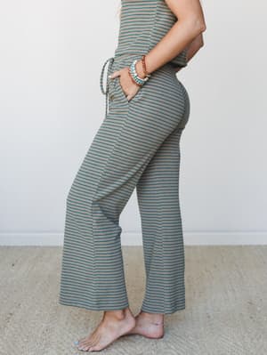 A side-profile shot of wide-leg striped pants with a drawstring waist, styled as a matching set with stacked beaded bracelets and a delicate anklet — relaxed and effortlessly put-together.