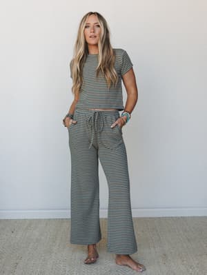 A matching striped two-piece set — cropped tee and wide-leg drawstring pants in a soft sage and teal stripe — styled with stacked beaded bracelets and bare feet for an easy, lived-in look.