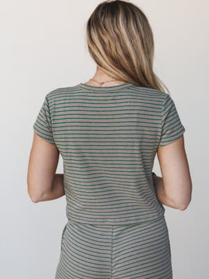 A back-facing shot of a fitted ribbed stripe tee in warm tan and teal, styled simply with a delicate gold necklace — the kind of easy top that anchors a whole outfit without trying.