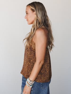 A side-profile shot of a model in a leopard-print cami with lace trim at the neckline, paired with denim and stacked beaded bracelets — the kind of top that makes jeans feel intentional.