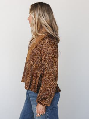 A side-profile shot of a leopard print blouse in warm camel and deep plum tones, styled with blue denim — the lace neckline trim and flowy peplum silhouette give it that effortless boho-meets-vintage energy.