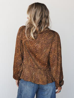 A back-view studio shot of a leopard print blouse in warm camel and plum tones, styled with medium-wash wide-leg jeans — the kind of top that does the heavy lifting without trying too hard.