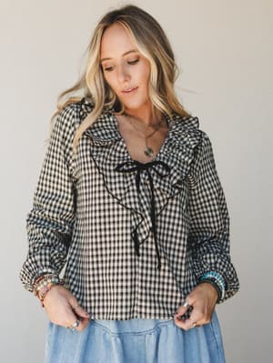 A gingham ruffle blouse in black and cream is styled with a tiered chambray skirt, layered gold necklaces, and a stack of beaded bracelets — the kind of outfit that looks effortless but definitely wasn't an accident.