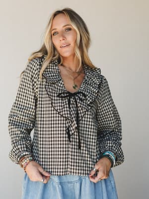 A gingham ruffle-front top in black and cream styled with a chambray tiered skirt, layered gold necklaces, and stacked beaded bracelets — the kind of outfit that feels vintage-inspired but totally wearable on a Tuesday.