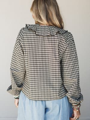 Shot from the back, this gingham blouse in black and cream pairs with light blue wide-leg pants — the ruffle collar and stacked bracelets give it that sweet-but-not-precious energy.