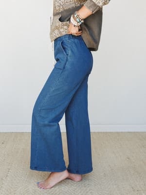 A side-profile shot of wide-leg denim pants with an elastic waistband, styled with a paisley print top and stacked boho bracelets — the kind of outfit that looks like you tried just enough.