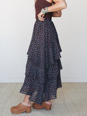 A tiered polka dot midi skirt in deep brown and dusty blue styled with a burgundy tank and tan wood-soled clogs, shot from the side with stacked turquoise bracelets adding that perfect boho finishing touch.