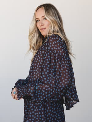 A sheer brown and slate blue polka dot blouse with dramatic ruffle cuffs and bell sleeves — the kind of top that looks equally at home at a wine bar or a weekend farmers market.