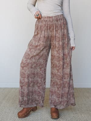 Flowy paisley wide-leg pants in a muted rose taupe paired with a striped long-sleeve top and wooden clogs — the kind of outfit that looks effortless but is doing a lot of quiet work.