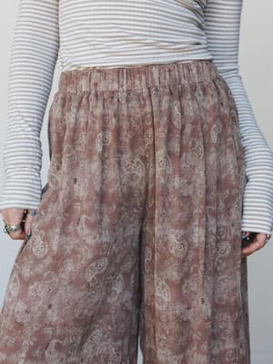 A close-up mid-shot of wide-leg paisley pants in a washed rose taupe, paired with a striped long-sleeve top — the kind of relaxed, expressive outfit that feels effortless without trying.
