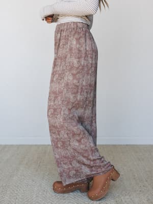 A side-profile shot of wide-leg paisley pants in a faded rose taupe, styled with a striped long-sleeve top and wooden clogs — the kind of outfit that looks intentional without trying too hard.