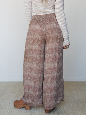 Shot from behind, a wide-leg paisley pant in rose taupe takes center stage — flowy and floor-grazing, styled with a striped ribbed long-sleeve and wooden clogs for that effortlessly collected boho feel.