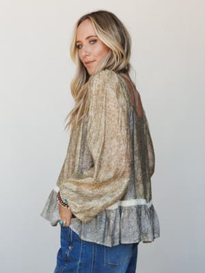 A flowy, sheer floral blouse in mustard olive and grey layered over denim jeans, styled with stacked boho bracelets — the kind of top that looks effortless but clearly wasn't an accident.