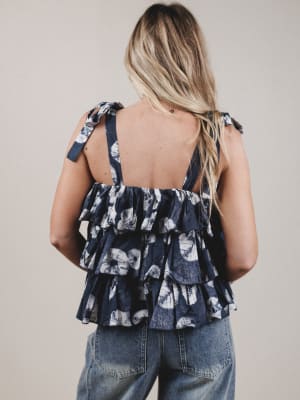 Woman wearing a navy floral tiered top with denim pants on a plain background