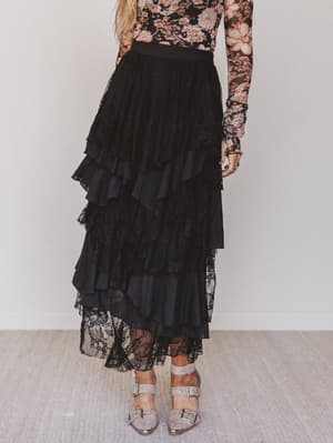 Person wearing a black ruffled skirt with a floral top against a white background