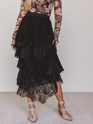 Person wearing a floral top and black ruffled skirt with lace details on a plain background