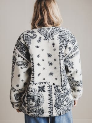 Person wearing a white cardigan with black paisley pattern on a plain background