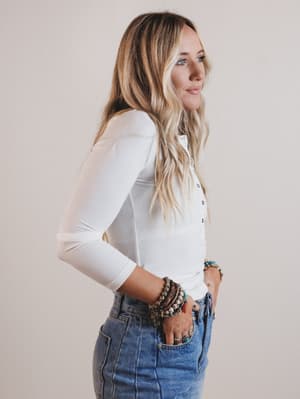 Woman wearing a white long-sleeve shirt and blue jeans with a neutral background