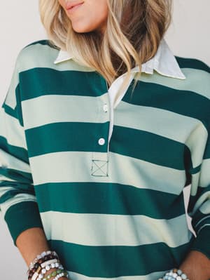 A close-up torso shot of a relaxed rugby-stripe pullover in hunter green and mint, layered over a white collared shirt — the kind of effortless, borrowed-from-the-boys look that feels as good as it looks.