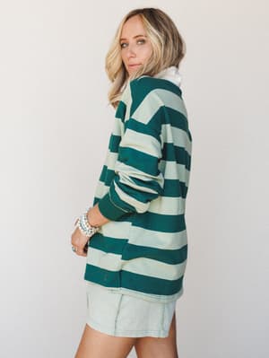 A model shot from the back-three-quarter angle showing an oversized striped rugby top in hunter green and sage paired with a light wash mini skirt — casual, cool, and effortlessly put-together.