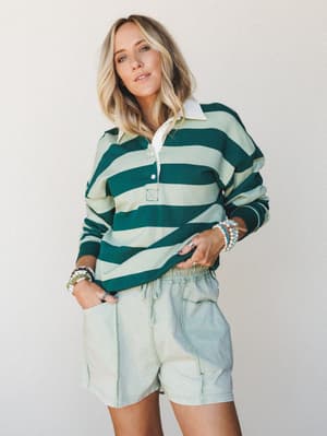 A relaxed, feel-good outfit pairing — an oversized rugby-stripe polo in forest and sage green worn with washed mint shorts, stacked with beaded bracelets for that effortless, put-together-without-trying energy.
