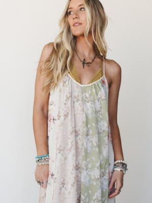 A flowy floral maxi dress in color-blocked cream and sage panels with a crochet V-neckline, styled with layers of beaded bracelets and a bird pendant necklace — effortless and a little dreamy.