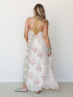 A flowy floral maxi dress shot from the back, showing off a crocheted mustard bodice with a strappy crossback detail — the kind of dress that makes you want to book a flight somewhere warm.