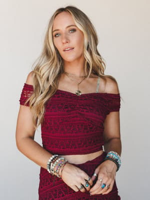 A burgundy lace crop top with an off-shoulder neckline is styled with a matching lace skirt, layered boho jewelry, and stacked beaded bracelets — the kind of outfit that feels intentional without trying too hard.