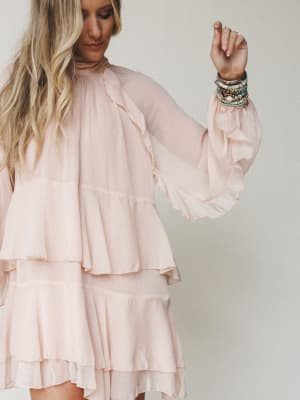 A flowy blush mini dress with tiered ruffles and bell sleeves, styled with a stack of beaded bracelets — the kind of dress that makes you want to twirl before you've even left the house.