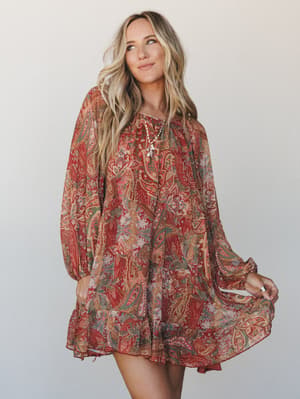 A flowy, oversized mini dress in a rich rust paisley print — the kind of dress that moves when you do and makes a Tuesday feel like something worth remembering.