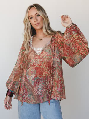 A flowy paisley blouse in warm rust and sage tones styled over a white lace cami with wide-leg jeans — effortlessly boho and the kind of top you reach for when you want to feel like yourself.