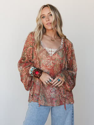 A relaxed paisley blouse in warm rust and sage layered over a lace cami, styled with light-wash jeans and stacked turquoise and silver jewelry — the kind of outfit that looks effortless but was definitely thought about.