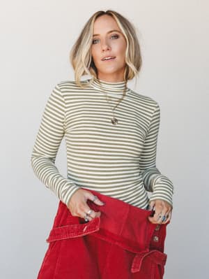 A striped olive and cream mock-neck long-sleeve top paired with red corduroy overalls — the kind of effortless color combo that looks like it took no thought but absolutely did.