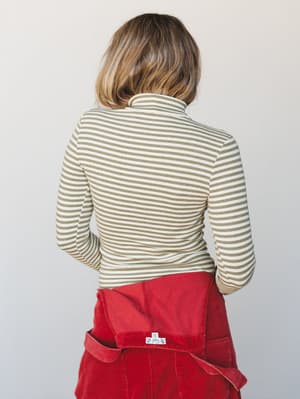 A back-view shot of a fitted olive and cream striped turtleneck layered over red corduroy overalls — the color combination feels intentional and a little vintage, like she raided the best thrift store in town.