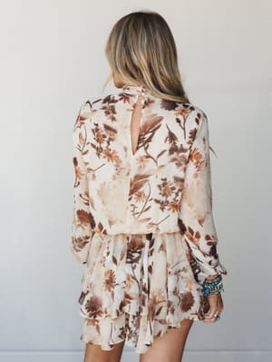A flowy floral mini dress shot from the back, showing off a keyhole closure, tiered ruffle skirt, and billowy long sleeves — styled with stacked turquoise and silver bracelets that give it that perfectly collected boho feel.