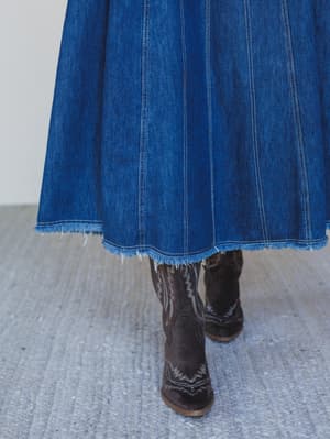 Person wearing a blue denim skirt and brown boots on a neutral background