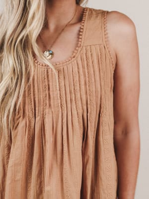 Close-up of a person wearing a beige sleeveless top with intricate detailing.
