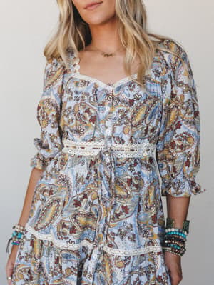 A powder blue paisley dress with cream lace trim details, styled with stacked boho bracelets — the kind of dress that feels equally at home at a farmers market or a summer wedding.