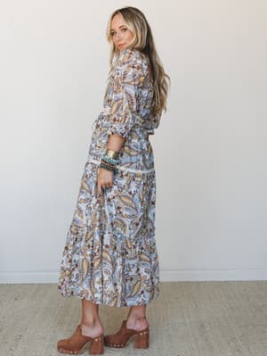 A paisley-printed midi dress in powder blue with warm earthy tones, styled with stacked boho bracelets and tan platform clogs — the kind of dress that makes a Tuesday feel intentional.
