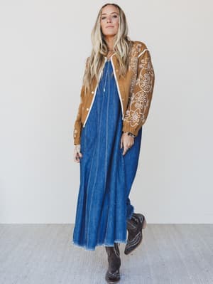 Person wearing a brown jacket with floral patterns and a blue denim dress against a white background