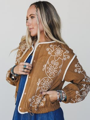 Woman wearing a brown jacket with white embroidery against a plain background