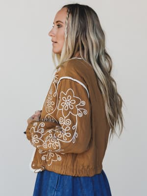 Woman wearing a brown jacket with white floral embroidery on a plain background