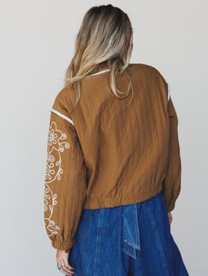 Person wearing a brown jacket with white embroidery on a plain background