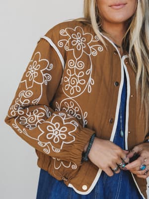 Brown jacket with white floral embroidery worn by a person against a neutral background