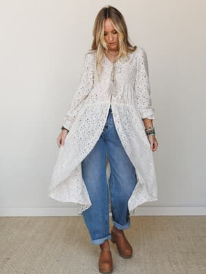 A cream eyelet maxi duster layered over relaxed boyfriend jeans and brown clogs — the kind of outfit that looks effortless but is clearly very intentional.
