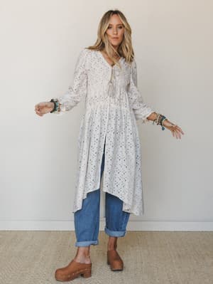 A long flowy printed duster layered over relaxed cuffed jeans and worn with tan clogs — the kind of outfit that looks effortless but was definitely thought about, stacked bracelets and all.