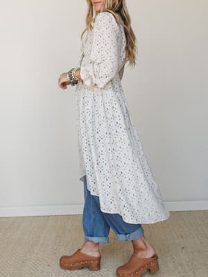 A long flowy duster dress in oatmeal layered over cuffed jeans and wood-soled clogs — the kind of outfit that looks effortless but was definitely thought about.