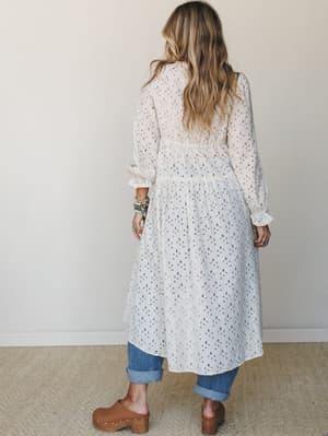 Shot from the back, this look layers a sheer tiered midi duster in oatmeal over cuffed blue jeans and tan clogs — effortlessly relaxed with a romantic, lived-in feel, finished with stacked turquoise and beaded bracelets.