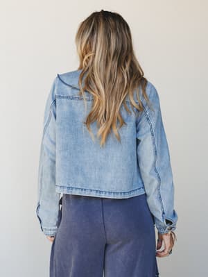 A back-view shot of a light wash cropped denim jacket paired with wide-leg dusty navy pants — easy, lived-in layering with a relaxed boho edge.