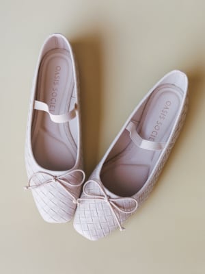 A pair of blush-toned woven ballet flats laid flat overhead, their basket-weave texture and dainty bow detail giving them that sweet-but-intentional quality you'd reach for on repeat.